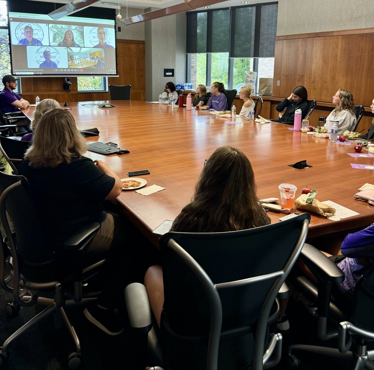 Participants gathered around a conference table with remote speakers on a presentation screen