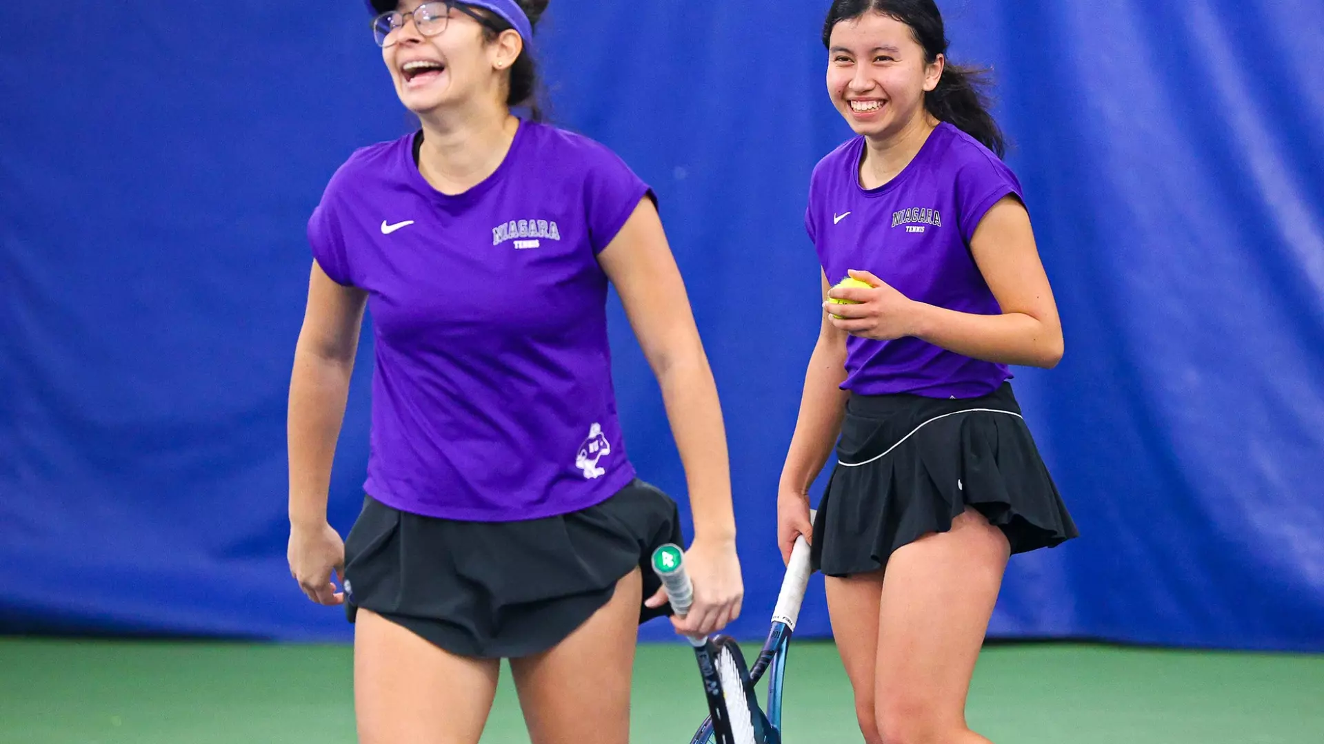 Two Niagara women’s tennis players smiling on an indoor court